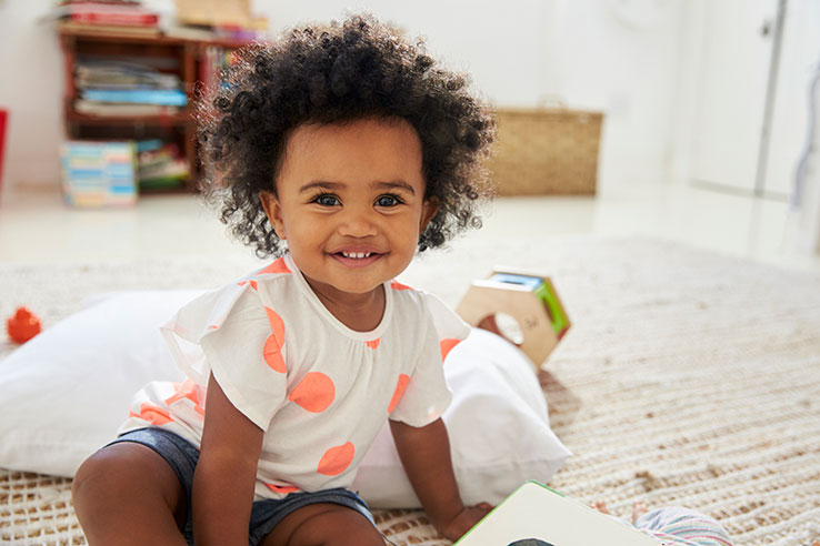 Happy baby girl playing with toys in playroom